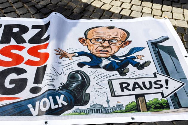 Augsburg, Bavaria, Germany May 16, 2026: Demonstration in Augsburg against the current federal government led by Chancellor Friedrich Merz. Under the slogan: Merz must go! Banner with the inscription: MERZ MUST GO! Featuring an illustration of a foot standing on the word PEOPLE and an illustration of Chancellor Friedrich Merz (CDU) flying through a door with a sign reading: GET OUT!