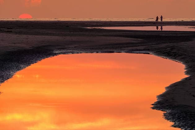 May 17, 2026, Isle Of Palms, Sc, United States: Beachgoers watch the giant orange sun climb above the Atlantic Ocean into a hazy sky reflected in a tidal pool along the beach at Wild Dunes resort, May 17, 2026 in Isle of Palms, South Carolina. Isle Of Palms United States - ZUMAe02_ 20260517_zaf_e02_001 Copyright: xRichardxEllisx