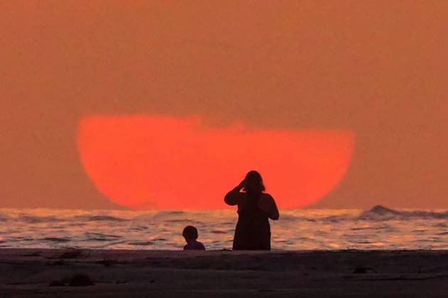 May 17, 2026, Isle Of Palms, Sc, United States: Beachgoers watch the giant orange sun climb above the Atlantic Ocean into a hazy sky at Wild Dunes resort, May 17, 2026 in Isle of Palms, South Carolina. Isle Of Palms United States - ZUMAe02_ 20260517_zaf_e02_003 Copyright: xRichardxEllisx