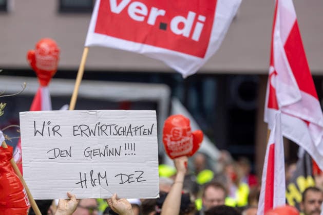 Bavaria-wide ver di trade strike starts with rally and demonstration, Nuremberg, 21 05 2026 Demonstrator holding a sign with the inscription Wir erwirtschaften den Gewinn H M DEZ at the central strike rally Ver di flags and red boxing glove balloons characterize the image of the protest crowd Nuremberg Kornmarkt Bavaria Germany 20260521-286A7541-M4000