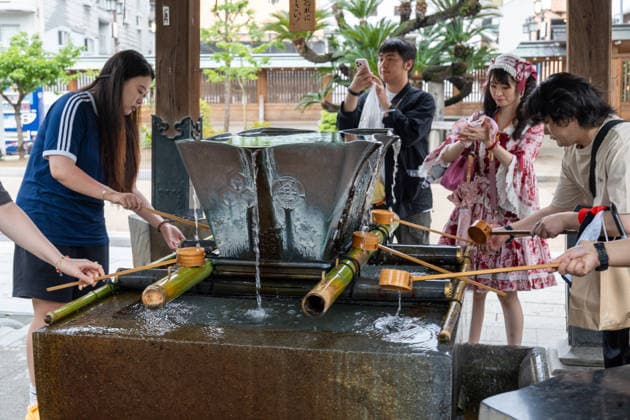 Fukuoka, Japan May 21, 2026: Visitors wash their hands at a traditional water basin at Kushida Shrine in Fukuoka, Japan. The scene depicts a typical purification ritual performed before entering the shrine and conveys Japanese culture, tradition, and religious customs.