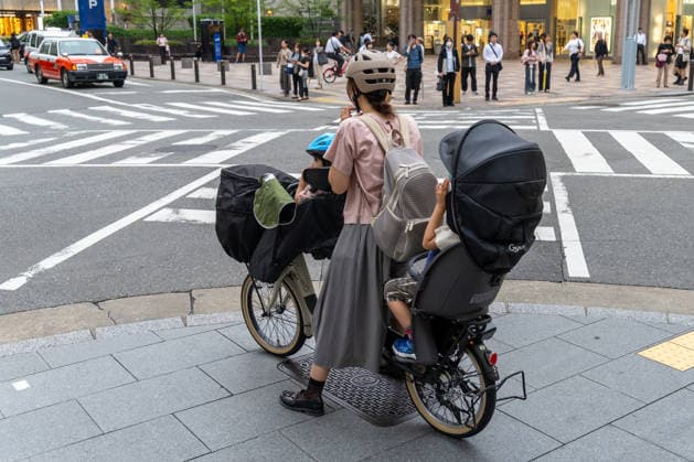 Fukuoka, Japan May 21, 2026: In Japan, a mother safely transports her children through urban traffic on a cargo bike. The image symbolizes sustainable mobility, everyday family life, cycling culture, and modern urban development.