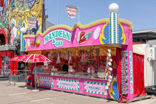 Freiburg im Breisgau GER, Volksfest, Freiburg im Breisgau, 24 05 2026 A colorful confectionery stand with the inscription Mandeln Co offers chocolate fruits, nut specialties and stomach bread at a fairground In the background you can see a fairground attraction with creepy motifs Copyright: xEibner-Pressefoto ThomasxHessx
