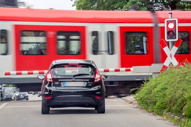 Munich S-Bahn passes gated level crossing, St. Andrews crosses flash red, train passes through, Ottobrunn near Munich, 30 May 2026 Germany, Ottobrunn near Munich, May 2026, gated level crossing, S-Bahn line S7 to Munich passes through, St. Andrews crosses flash red, cars wait in front of the barrier, midday, public transport, loca