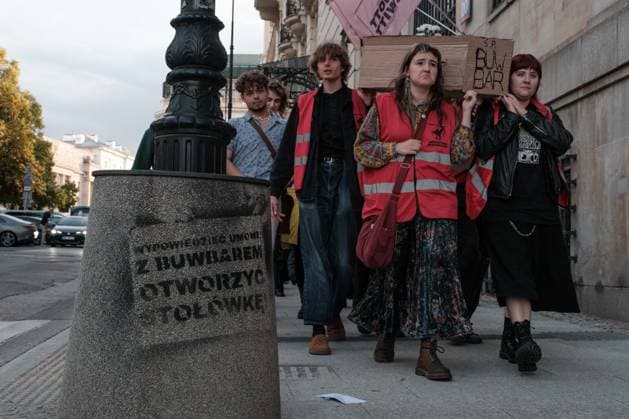 June 12, 2026, Warsaw, Masovian Voivodeship, Poland: Student activists carry a symbolic cardboard coffin and white flowers during a mock funeral procession doubling as a students demonstration welcoming the recent closure of the University of Warsaw s premium food hall, BUWBAR, located in the main library on campus. The establishment closed suddenly after only a month of operation following intense protests by students, who were promised an affordable student s canteen by the university s rector but were instead given an expensive food hall offering premium meals beyond student budgets. The graffiti on the trash bin on the left reads terminate the contract with BUWBAR and open a canteen! Warsaw Poland - ZUMAk204 20260612_zip_k204_030 Copyright: xRomanxKozielx