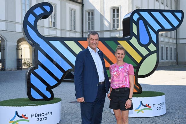 Markus SOEDER, Minister-President of Bavaria and CSU Chairman, Jessica BREDOW WERNDL in front of the mascot, Olympia the Dachshund, at a press event held as part of the invitation extended by the leading Olympic federations to present the detailed bid concept for Munich 20XX on Thursday, June 18, 2026, in front of Nymphenburg Palace,detected_source_language