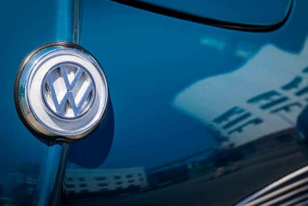 Close-up of the VW logo on the hood of a Karmann Ghia Coupé. The VW Osnabrück plant is reflected in the blue paint. 11 07 2026. Symbolic image of VW Osnabrück