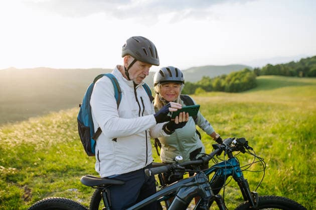 Senior couple planning cycling route with smartphone during e-bike trip. Senior couple planning cycling route with smartphone during e-bike trip in nature. model released