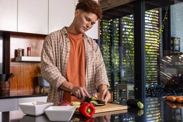 Man slicing zucchini on cutting board in home kitchen with peppers, eggplant, white bowls, model released, property released, 07.06.2024 06:00:00, 6430714 Copyright: xIDS-250919xcreatorid:x0x 6430714