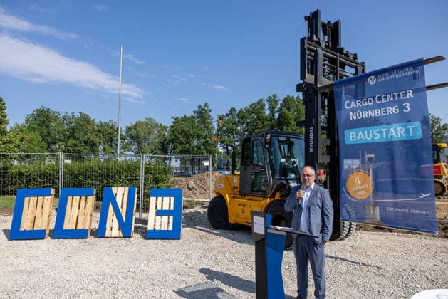 Groundbreaking for Cargo Center 3 at Nuremberg Airport, Nuremberg, August 4, 2026 A speaker addresses the audience from the podium at the groundbreaking ceremony for the new Nuremberg Cargo Center 3 (CCN 3) at Nuremberg Airport. In the background are a forklift and a promotional banner for the construction project. The expansion of 20260804-286A4179-M4000