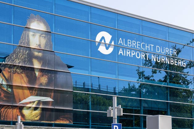 Nuremberg Airport, August 4, 2026: The facade of the Albrecht Dürer Airport Nuremberg featuring a large-scale self-portrait by Albrecht Dürer and the airport’s logo. The glass facade of the terminal building reflects the blue sky. Nuremberg Airport, Bavaria, Germany 20260804-1V9A6684-M4000