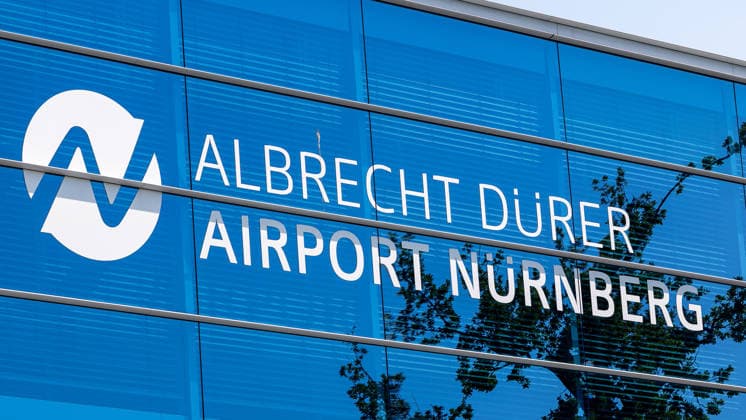 Nuremberg Airport, August 4, 2026 The Albrecht Dürer Airport Nuremberg lettering and logo on the facade of the terminal building The blue glass facade reflects the trees and the sky Nuremberg Airport, Bavaria, Germany 20260804-1V9A6686-M4000