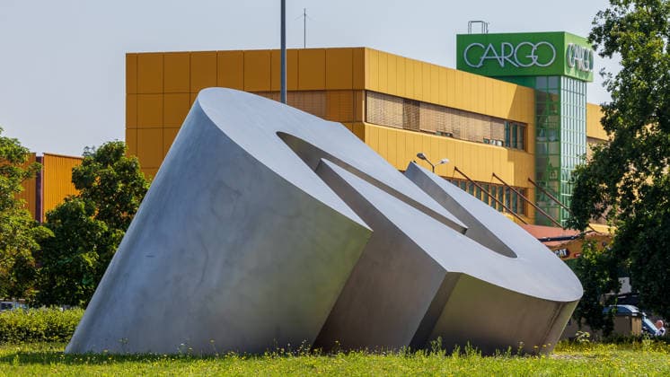 Construction Begins on Cargo Center 3 at Nuremberg Airport, Nuremberg, August 4, 2026 A striking metal sculpture of the airport logo stands in the foreground of the site where construction of the new Cargo Center 3 at Nuremberg Airport is beginning. In the background, the facade of the existing Cargo Center 1 can be seen, featuring the word Cargo. Nuremberg Airport, Ba 20260804-1V9A6676-M4000