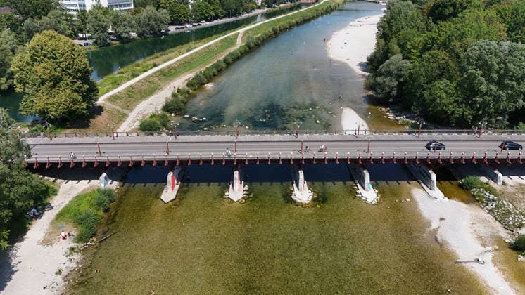A summer day in Munich, the state capital. Here is a view of the Thalkirchner Bridge, a road bridge over the Isar River and the parallel Isar Werkkanal, which will be closed for two years starting in 2027 due to renovation, maintenance, traffic congestion, detours, neighborhoods, the zoo, and frustrated residents