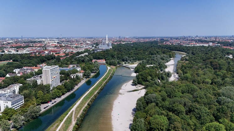 A summer day in Munich, the state capital. Here is a view of the Isar River and the Isar Werkskanal, as well as the Flaucher—a swimming area, pebble beach, and the Munich skyline—looking north: cityscape, sea of buildings, recreational area, sunbathing, swimming, cooling off