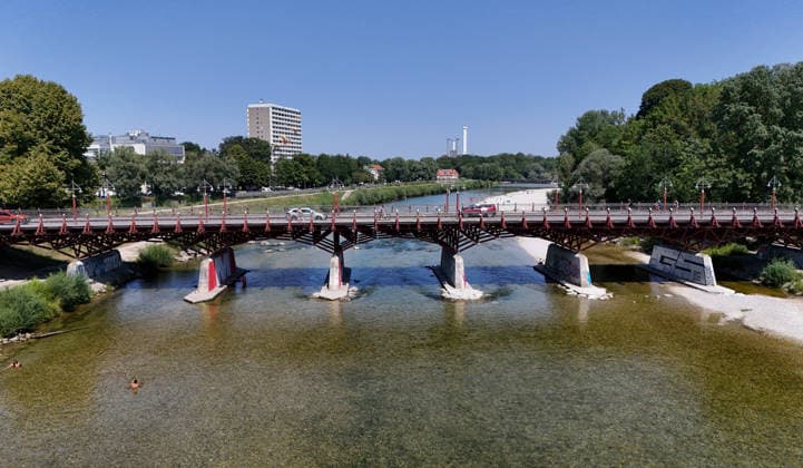 A summer day in Munich, the state capital. Here is a view of the Thalkirchner Bridge, a road bridge over the Isar River and the parallel Isar Werkkanal, which will be closed for two years starting in 2027 due to renovation, maintenance, traffic congestion, detours, neighborhoods, the zoo, and frustrated residents
