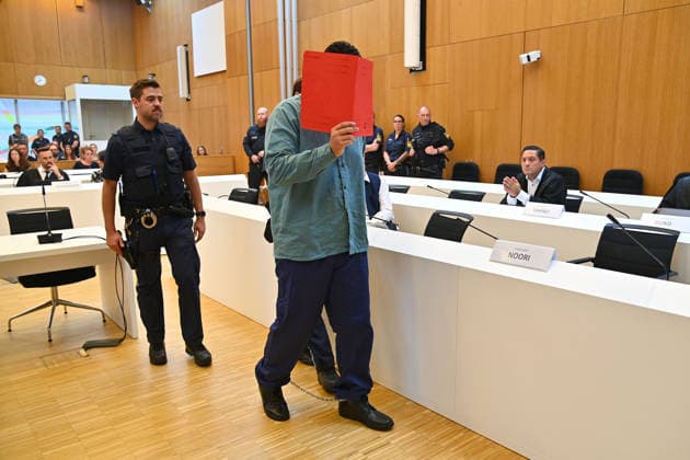 The defendant is escorted into the courtroom by court officers. The verdict in the criminal case against Farhad Noori for murder, among other charges, related to the Seidlstrasse incident will be handed down on August 6, 2026, at the Munich Higher Regional Court.