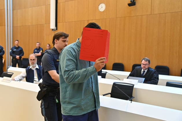 The defendant is escorted into the courtroom by court officers. The verdict in the criminal case against Farhad Noori for murder, among other charges, related to the Seidlstrasse incident will be handed down on August 6, 2026, at the Munich Higher Regional Court.