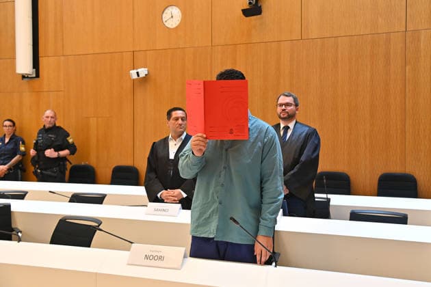 The defendant in the courtroom hides his face behind a binder. Judgment in the criminal case against Farhad Noori for murder, among other charges, on Seidlstrasse on August 6, 2026, before the Munich Higher Regional Court