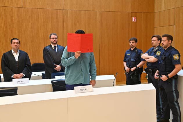 The defendant in the courtroom hides his face behind a binder. Judgment in the criminal case against Farhad Noori for murder, among other charges, on Seidlstrasse on August 6, 2026, before the Munich Higher Regional Court