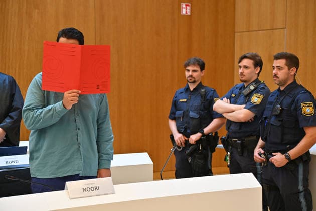 The defendant in the courtroom hides his face behind a binder. Judgment in the criminal case against Farhad Noori for murder, among other charges, on Seidlstrasse on August 6, 2026, before the Munich Higher Regional Court
