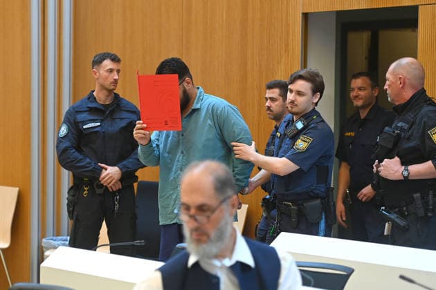 The defendant is escorted into the courtroom by court officers. The verdict in the criminal case against Farhad Noori for murder, among other charges, related to the Seidlstrasse incident will be handed down on August 6, 2026, at the Munich Higher Regional Court.