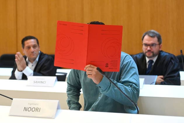 The defendant in the courtroom hides his face behind a binder; behind him are his attorneys. Verdict in the criminal trial against Farhad Noori for murder, among other charges, on Seidlstrasse on August 6, 2026, before the Munich Higher Regional Court