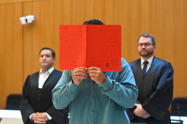 The defendant in the courtroom hides his face behind a binder; behind him are his attorneys. Verdict in the criminal trial against Farhad Noori for murder, among other charges, on Seidlstrasse on August 6, 2026, before the Munich Higher Regional Court