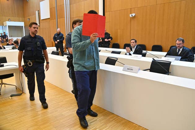 The defendant is escorted into the courtroom by court officers. The verdict in the criminal case against Farhad Noori for murder, among other charges, related to the Seidlstrasse incident will be handed down on August 6, 2026, at the Munich Higher Regional Court.