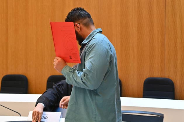 The defendant in the courtroom hides his face behind a binder. Judgment in the criminal case against Farhad Noori for murder, among other charges, on Seidlstrasse on August 6, 2026, before the Munich Higher Regional Court