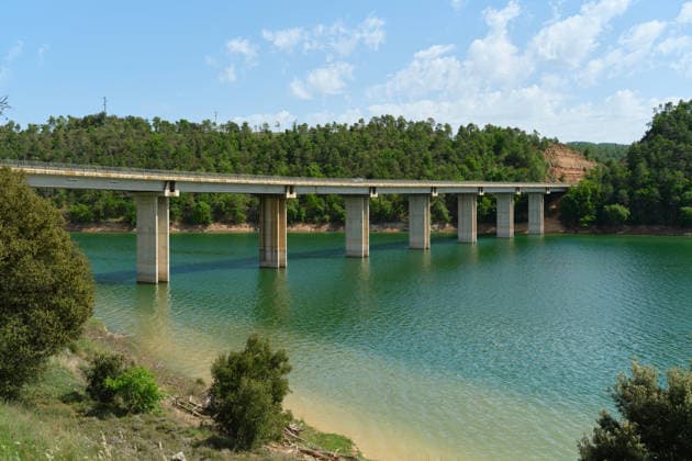 Betonbrücke vor dem Hintergrund eines türkisfarbenen Stausees. A horizontal outdoor shot of a long concrete bridge with high support pillars spanning over a turquoise water reservoir surrounded by lush green hills, ideal for infrastructure and travel designs. (License=RF) Copyright: xZoonar.com EkaterinaxMitsenx 25333596