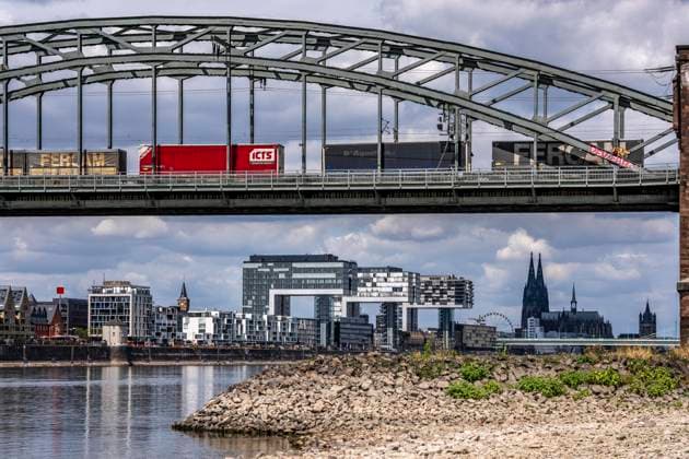 Low water levels in the Rhine near Cologne; view from the right bank of the Rhine across the Poller Wiesen, looking north toward the Südbrücke, the railroad bridge, freight train, downtown skyline with the cathedral; inland waterway shipping is severely restricted, with only a few ships operating—and those with greatly