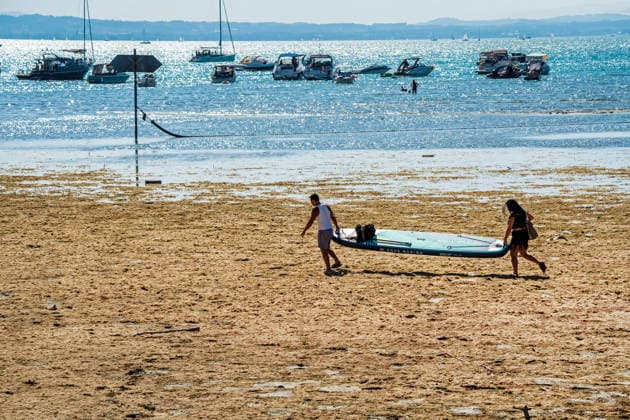 Two water sports enthusiasts carry their large stand-up paddleboard across th
