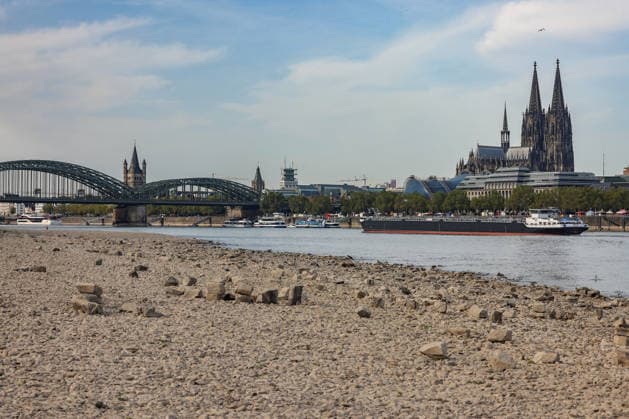 Summer in the Rhineland: View of the Rhine near Cologne (Deutz). The Rhine in Cologne is at low water levels due to persistent drought. In the background, the Hohenzollern Bridge is on the left and Cologne Cathedral is on the right. A ship is passing by. Summer in the Rhineland on August 9, 2026 in Cologne, Germany
