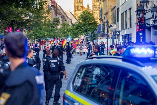 Police operation during the Monday demonstration by Team Menschenrechte and counter-protests, Nuremberg, 10 087 2026 Police officers escort a demonstration march by Team Menschenrechte through Karolinenstraße. A police vehicle with its blue lights flashing is parked at the edge of the pedestrian zone; flags and participants in the march can be seen in the background. Nurembe 20260810-286A4982-M4000