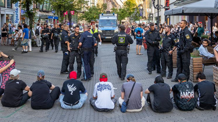 Police operation during the Monday demonstration by Team Menschenrechte and counter-protests, Nuremberg, 10 087 2026 On Karolinenstraße, a group of counter-protesters is sitting down to block the march organized by Team Menschenrechte. Numerous police officers in tactical gear stand between the seated protesters and passersby; in the background is 20260810-6V2A0667-M4000