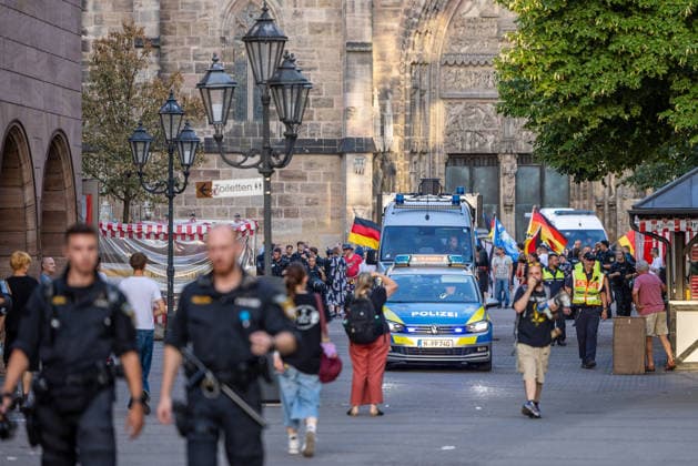 Police operation during Monday demonstration by Team Menschenrechte and counter-protests, Nuremberg, 10 087 2026 Police officers escort a demonstration march by Team Menschenrechte and counter-protesters on Karolinenstraße. A police patrol car with its blue lights flashing drives through the pedestrian zone amid demonstrators carrying German flags. Nuremberg, Bavari 20260810-286A4960-M4000