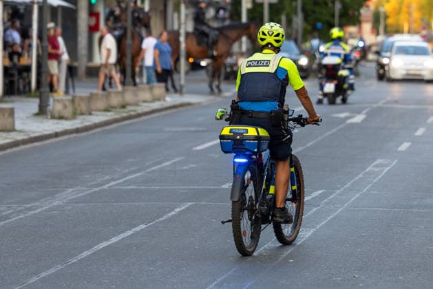 Police operation during the Monday demonstration organized by Team Menschenrechte and counter-protests, Nuremberg, August 10, 2026. A police officer on a bicycle is directing traffic; mounted police and a police motorcycle can be seen in the background. Nuremberg, Bavaria, Germany 20260810-286A5010-M4000