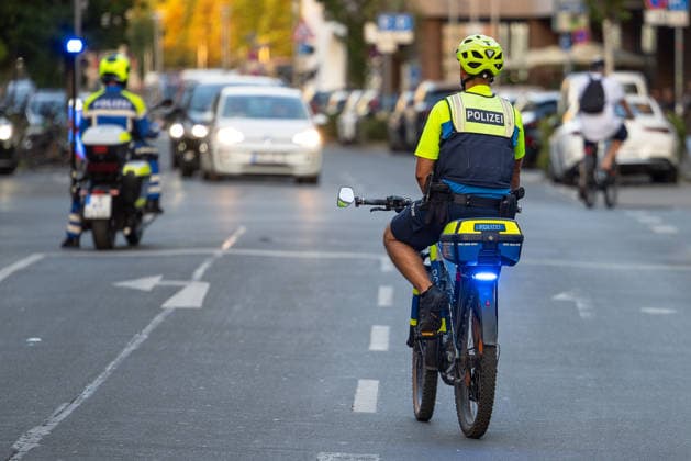 Police operation during the Monday demonstration by Team Menschenrechte and counter-protests, Nuremberg, 10 087 2026 Police officers on bicycles and motorcycles direct traffic during an operation. A bicycle patrol with its blue lights flashing rides through traffic, while another officer on a police motorcycle follows in the background. Nuremberg, Bavaria, Germany 20260810-286A5017-M4000