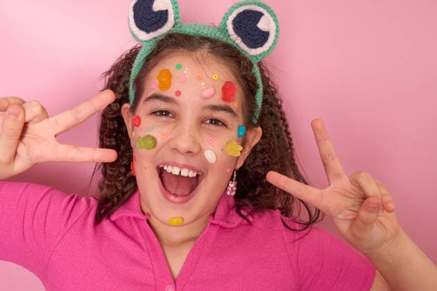 Fröhliches Kind mit buntem Gesicht aus Süßigkeiten und lustigen Accessoires vor einem leuchtend rosa Hintergrund Cheerful Child with Colorful Candy Face Art and Fun Accessories in a Bright Pink Setting (License=RF) ,model released, Symbolfoto Copyright: xZoonar.com NatashaxZakharovax 25418792 ,model released, Symbolfoto ,property released