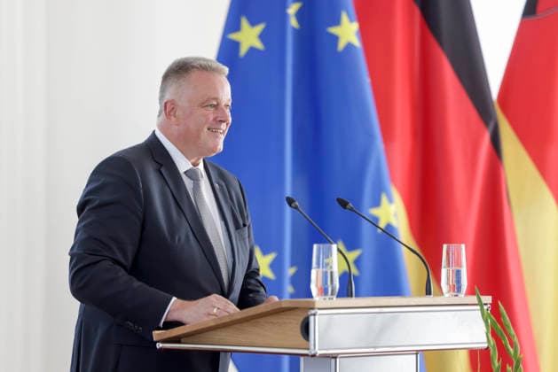 Prime Minister Gordon Schnieder at the lectern in front of flags during a ceremony to confer professional titles at the State Chancellery of Rhineland-Palatinate, August 26, 2011
