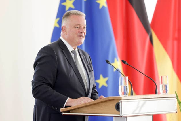 Prime Minister Gordon Schnieder at the lectern in front of flags during a ceremony to confer professional titles at the State Chancellery of Rhineland-Palatinate, August 26, 2011