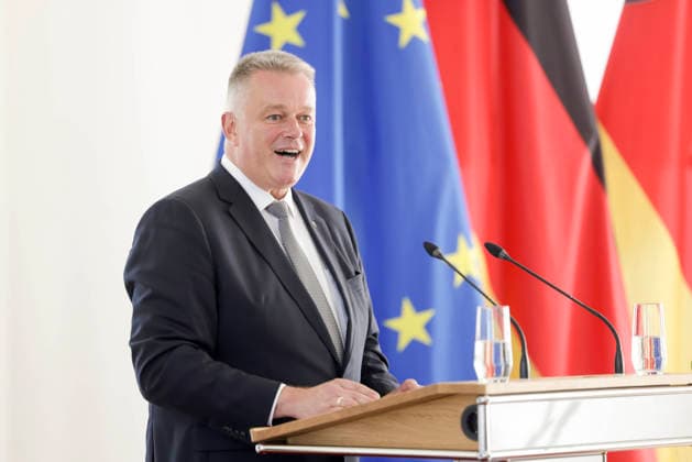 Prime Minister Gordon Schnieder at the lectern in front of flags during a ceremony to confer professional titles at the State Chancellery of Rhineland-Palatinate, August 26, 2011