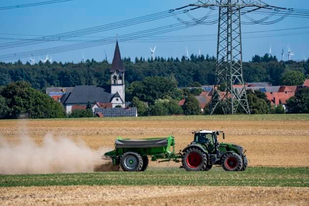 A tractor equipped with a mineral fertilizer spreader is working a harvested grain field, spreading mineral fertilizer and lime to improve soil quality for future use and planting, at Marsberg Meerhof, North Rhine-Westphalia, Germany—field work