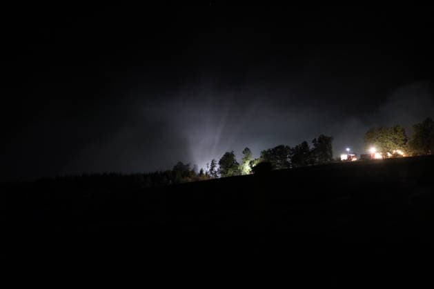 Marsberg, North Rhine-Westphalia, Germany, Europe: A wide-angle shot of a nighttime forest fire operation near the Diemel Dam. Thick smoke rises above the forest and is illuminated by spotlights and emergency lights. Fire trucks and emergency personnel continue firefighting operations along the edge of the forest throughout the night. Copyright: xAymanxAlahmedx