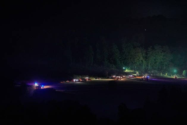 Helminghausen, Marsberg, North Rhine-Westphalia, Germany, Europe Wide-angle shot of a nighttime forest fire operation featuring numerous fire trucks and emergency personnel in an open area at the edge of the forest. Mobile lighting and blue lights mark the staging area, while firefighters continue firefighting operations and coordinate the response in r Copyright: xAymanxAlahmedx