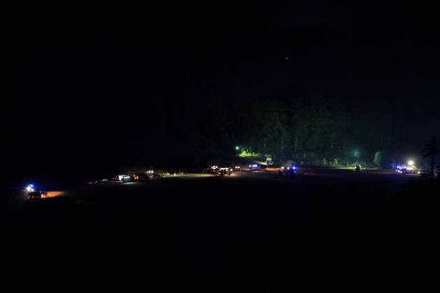Helminghausen, Marsberg, North Rhine-Westphalia, Germany, Europe Wide-angle shot of a nighttime forest fire operation featuring numerous fire trucks and emergency personnel in an open area at the edge of the forest. Blue lights and mobile floodlights illuminate the expansive staging area, while firefighters continue firefighting oper Copyright: xAymanxAlahmedx