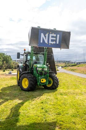 A banner attached to a tractor bearing the words NEI ( No ) stands on a busy street i
