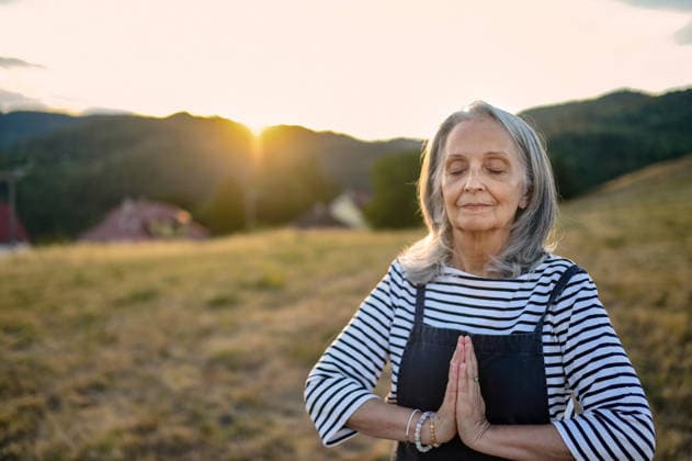 Senior woman practicing meditation outdoors in peaceful countryside. Senior woman taking care of body and mind during outdoor wellness routine. model released