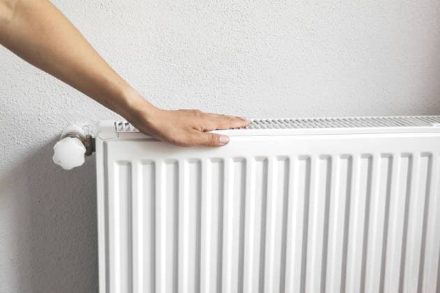 Eine menschliche Hand berührt den weißen Metallheizkörper gegen eine helle Wand, überprüft die Wärme während der Heizperiode und steht für Wohnkomfort, Energieeffizienz und Raumklimakonzept Human hand touching white metal radiator against light wall, checking warmth during heating season, symbolizing home comfort, energy efficiency and indoor climate control concept Copyright: imageBROKER EvgeniiaxGordeeva ibxiqx18667032.jpg